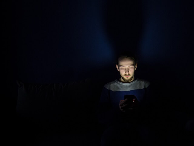 真っ暗な部屋で寝っ転がりながらスマホを見る人。