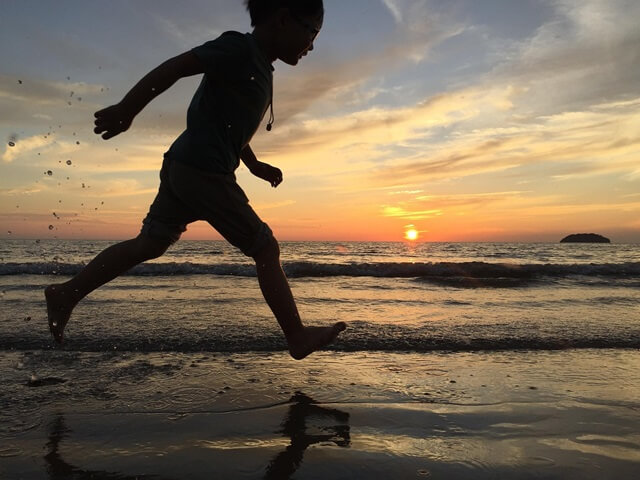 太陽が昇る中、砂浜を駆け回る人。
