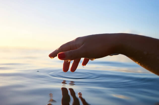 朝日で照らされた海面に手をかざし、小さな波紋が生まれる